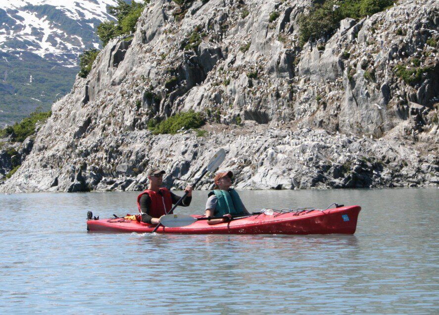 two people in a tandem kayak along a rocky coast