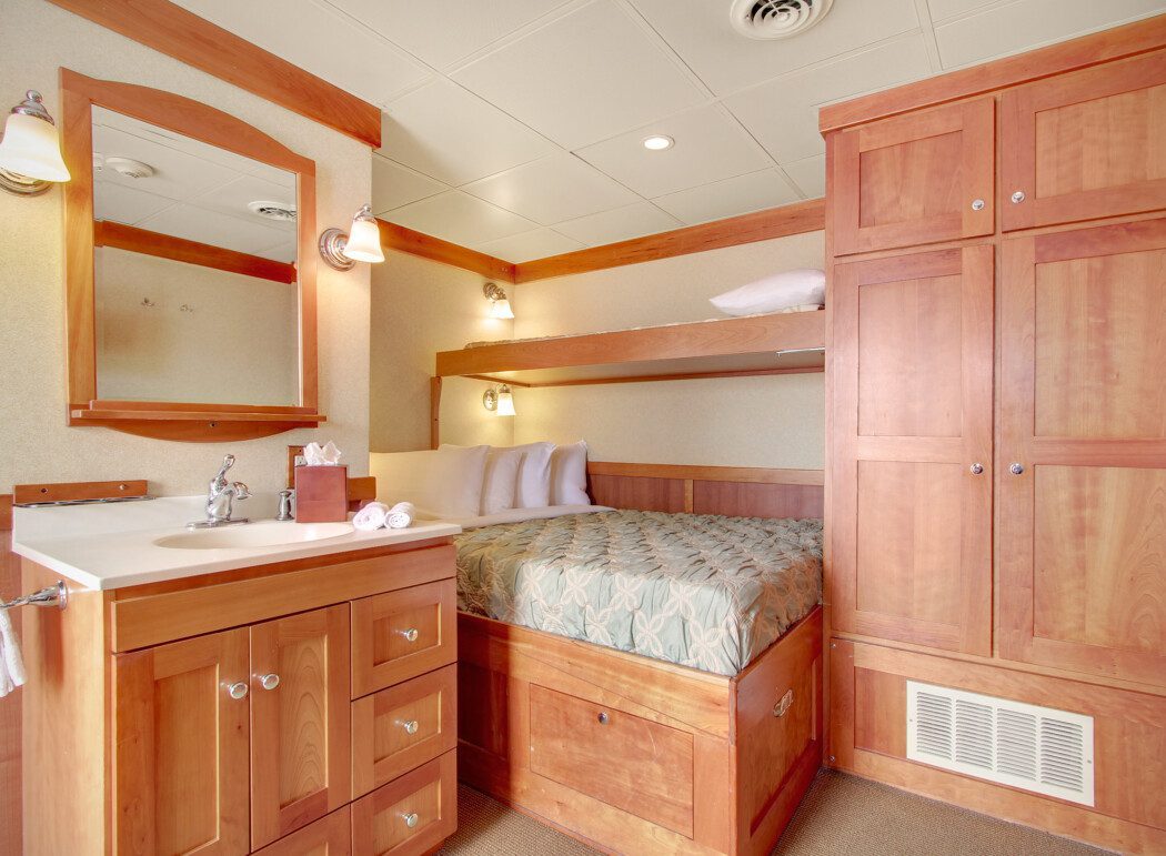 the inside of a cruise ship cabin, showing wood-paneled cabinets, a bed and a sink