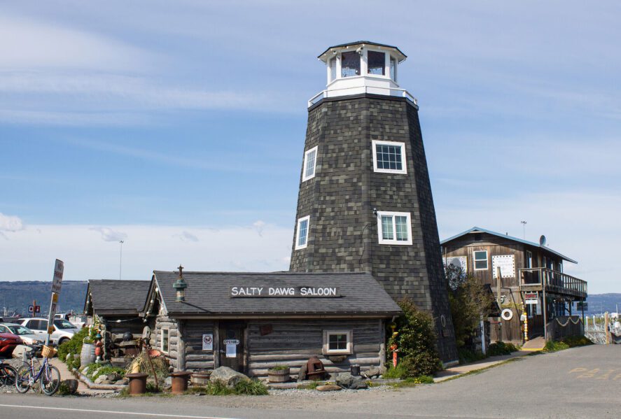 a saloon composed of a log cabin and a lighthouse tower on a beachfront