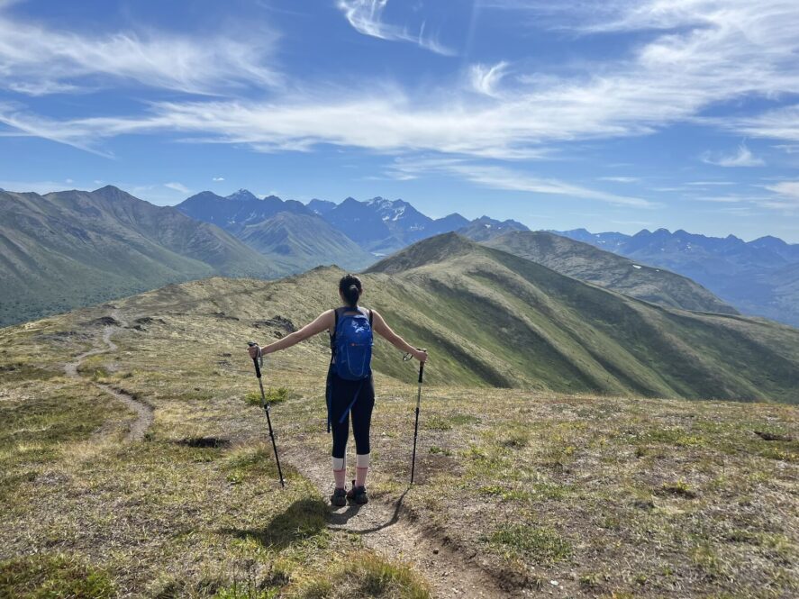 A person with trekking poles hiking along an alpine trail in Alaska