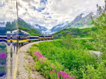 the blue and yellow Alaska Railroad train traveling past a glacier.
