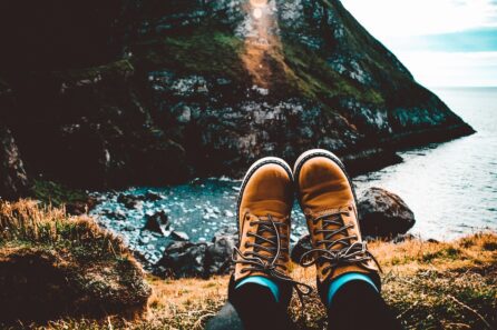 Person's feet wearing tan hiking boots, resting on a grassy cliff